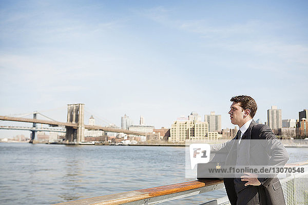 Nachdenklicher Geschäftsmann schaut weg  während er am Geländer gegen Brücken steht