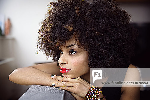 Thoughtful woman with curly hair resting on sofa at home