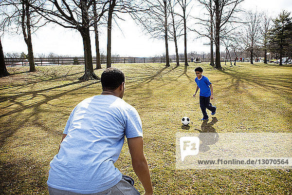 Vater spielt Fussball mit Sohn auf dem Spielfeld im Park