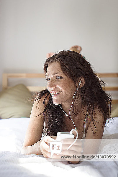 Nachdenkliche Frau  die Musik hört  während sie zu Hause im Bett liegt
