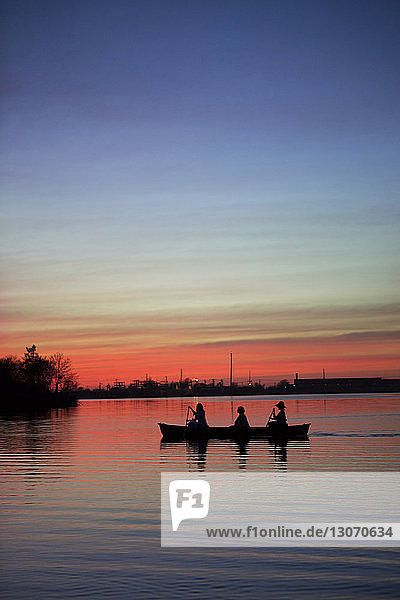 Silhouettenfreunde rudern bei Sonnenuntergang Boot auf dem See gegen den Himmel