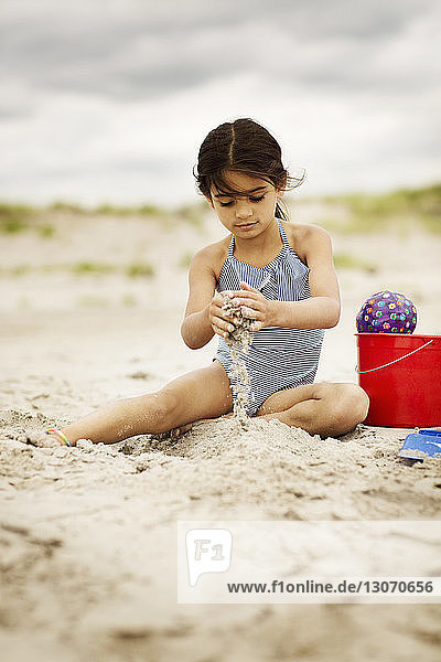 Mädchen spielt mit Sand  während sie am Strand sitzt