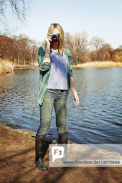Woman photographing while standing by lake
