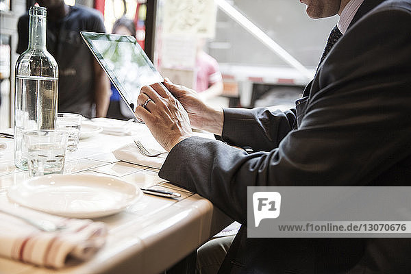 Side view of businessman using tablet computer while sitting at table in restaurant