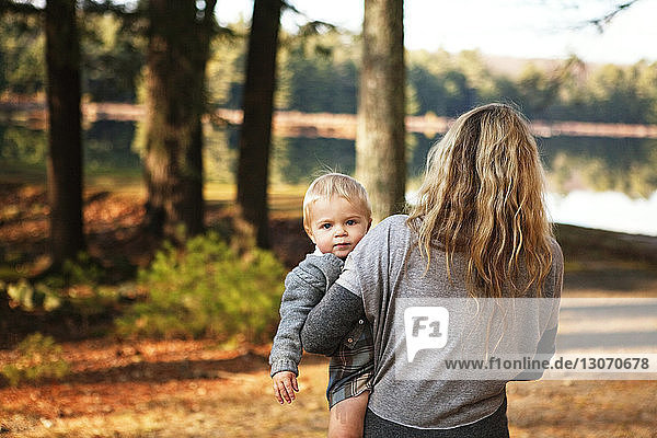 Rear view of woman carrying baby while walking on field