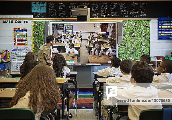 Rear view of students looking at photographs on projection screen while sitting at desk in classroom