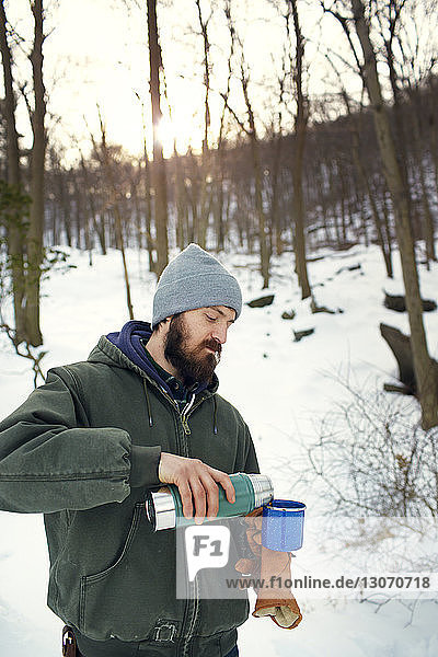 Man pouring drink while standing on snow covered field in forest