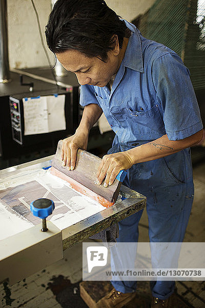 Hochwinkelansicht eines Mannes  der in der Werkstatt Tinte auf einen Rahmen drückt