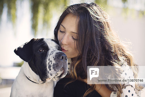 Junge Frau mit langen Haaren küsst Hund an sonnigem Tag