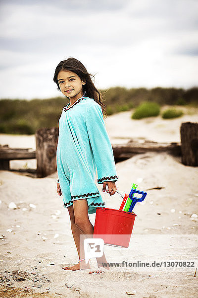 Porträt eines lächelnden Mädchens mit Sandkübel und Schaufeln am Strand