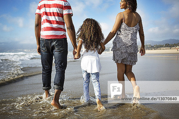 Rückansicht einer Familie  die am Strand am Ufer spazieren geht