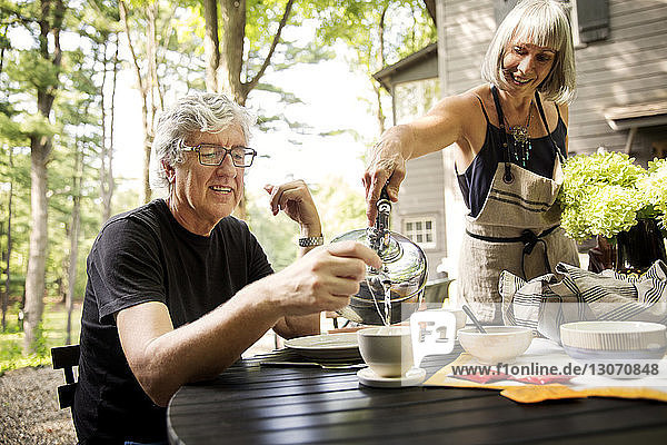 Lächelnde Frau schenkt dem älteren Mann am Tisch im Hof Kaffee ein