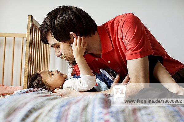 Father looking at daughter while lying on bed at home