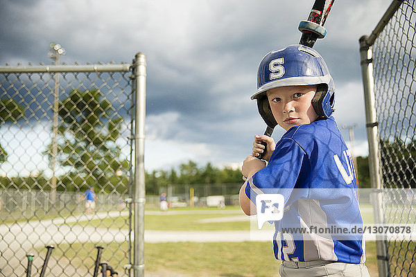 Portrait of boy practicing on field against cloudy sky