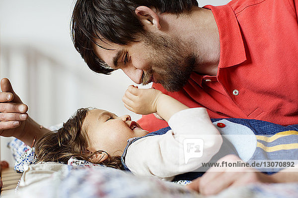 Happy father looking at daughter while lying on bed at home