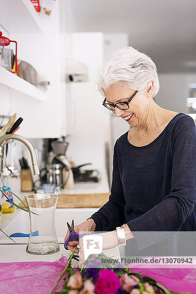 Senior woman cutting flowers stem at home