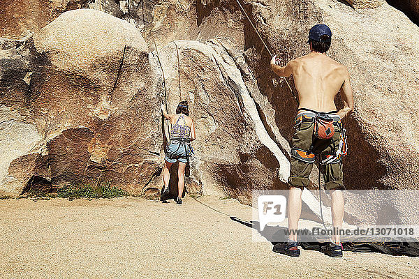 Rückansicht von Freunden  die sich an einem sonnigen Tag auf das Klettern am Fels vorbereiten
