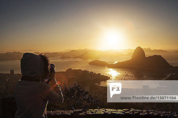 Frau fotografiert den Zuckerhut-Berg  während sie bei Sonnenuntergang am Beobachtungspunkt steht
