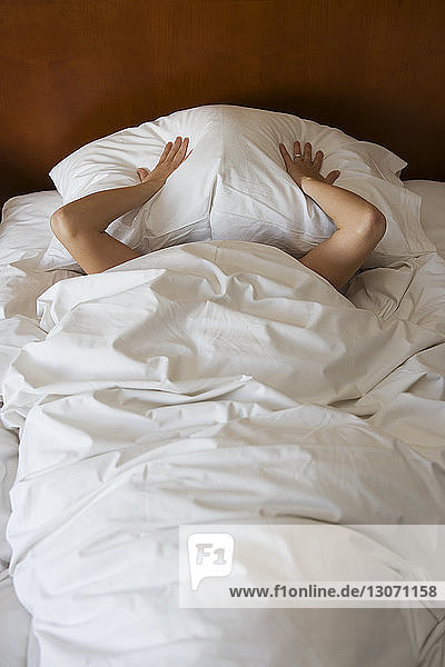 Hochwinkelansicht einer Frau  die ihr Gesicht mit einem Kissen auf dem Bett bedeckt