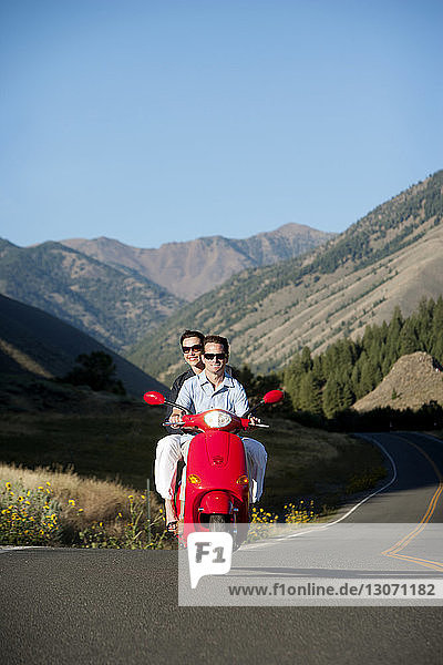 Glückliches Paar fährt mit dem Motorroller gegen die Berge