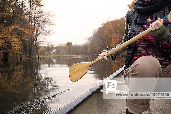 Midsection of woman rowing boat on lake at forest during winter
