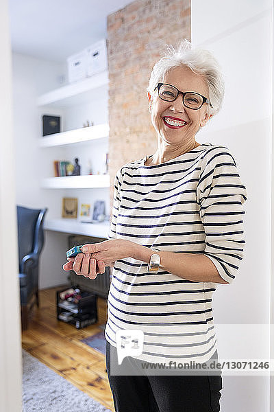 Porträt einer älteren Frau  die ein Mobiltelefon in der Hand hält  während sie zu Hause steht