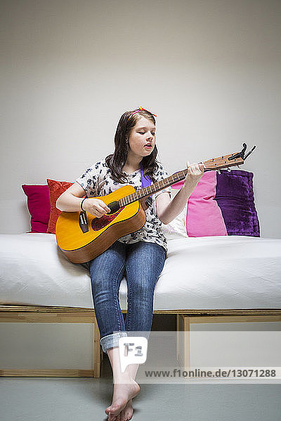 Mädchen spielt Gitarre  während sie zu Hause auf dem Sofa sitzt