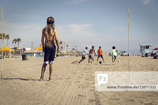 Kinder spielen Fussball am Strand gegen den Himmel
