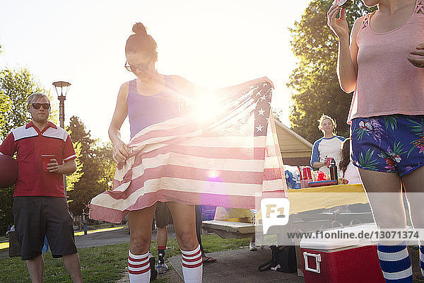 Frau hält amerikanische Flagge  während sie mit Freunden im Park steht