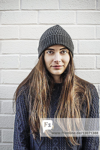 Portrait of woman wearing knit hat standing against brick wall