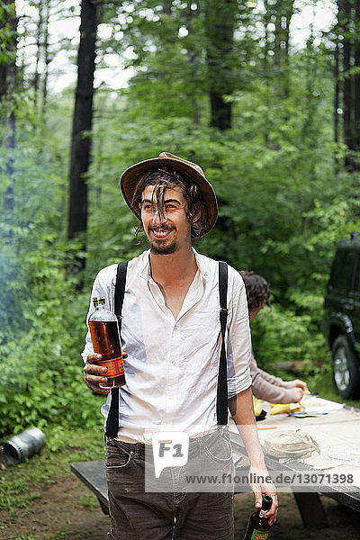 Man holding bear bottles looking away while standing in forest