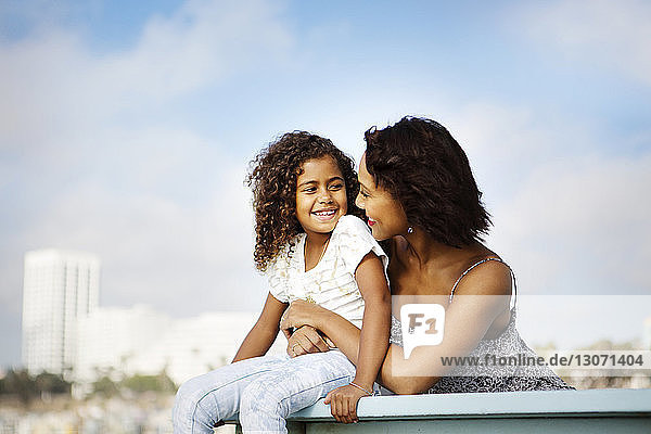 Frau umarmt Tochter  während sie sich am Geländer am Pier gegen den Himmel entspannt