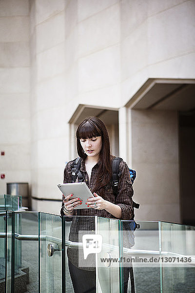 Frau benutzt Tablet-Computer  während sie am Bahnhof am Geländer steht