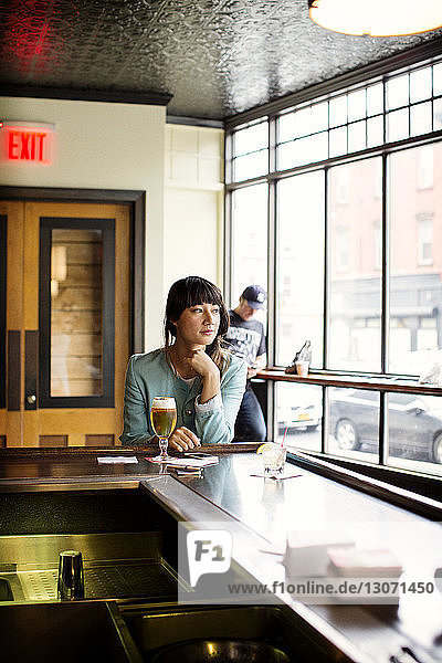 Thoughtful woman looking away while leaning on table in bar