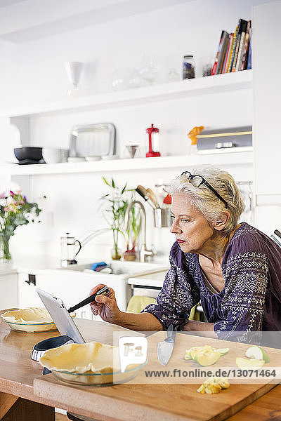 Frau benutzt Tablet-Computer beim Apfelkuchenbacken in der Küche