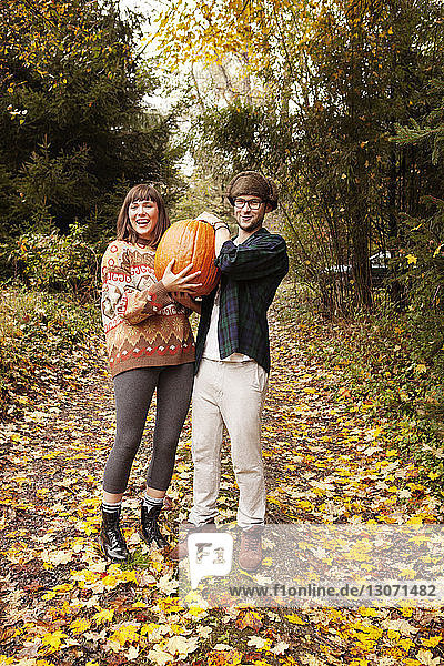 Portrait of couple carrying Halloween pumpkin while standing on field