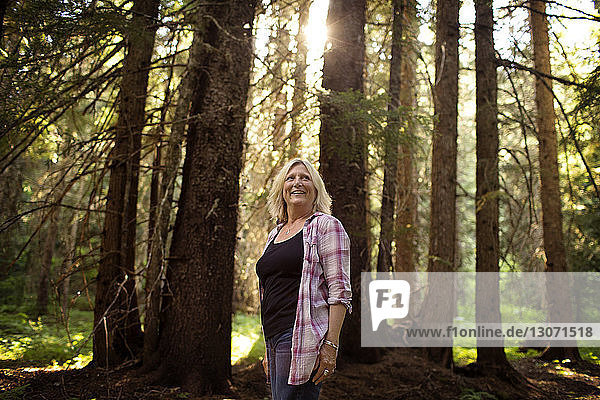 Glückliche reife Frau steht an Bäumen im Wald