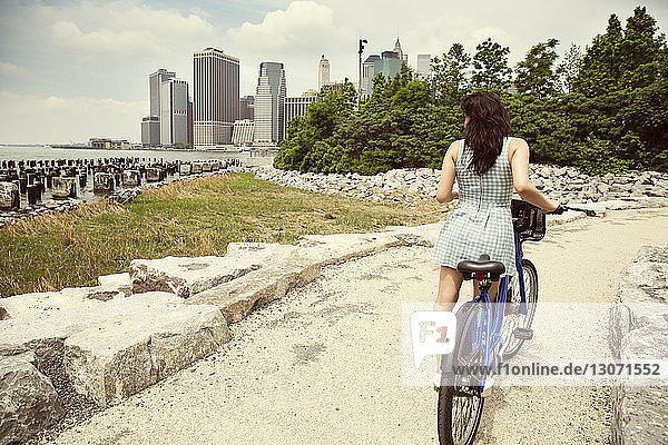 Rear view of woman with bicycle standing on pathway by river in city