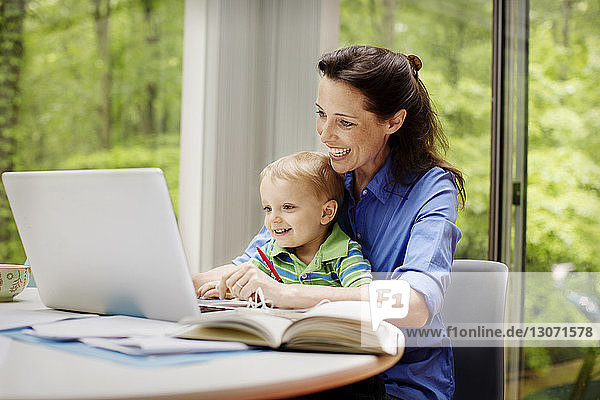 Glückliche Mutter mit Sohn mit Laptop am Tisch vor dem Fenster