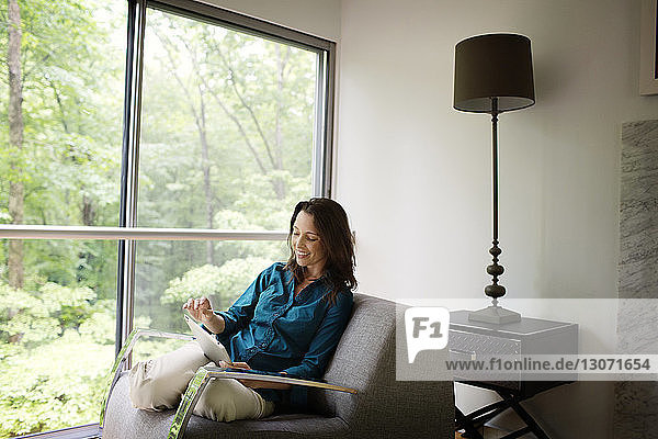 Lächelnde Frau mit Tablet-Computer zu Hause auf dem Sofa sitzend