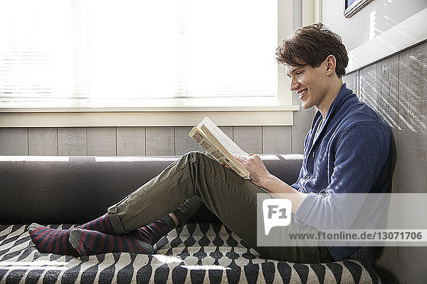 Side view of man smiling while reading book at home