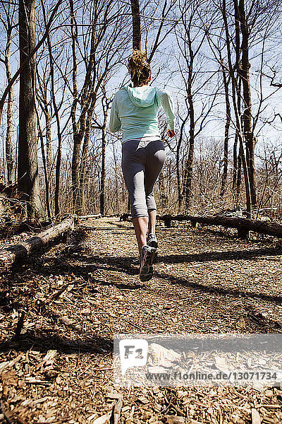 Rear view of woman jogging on dirt road amidst bare trees