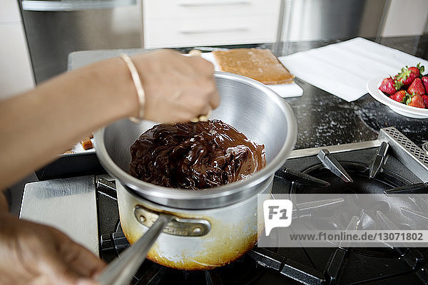 Ausgeschnittenes Bild Frau beim Hinzufügen von Lebensmitteln in geschmolzener Schokolade