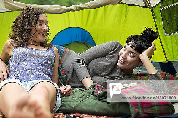 Happy friends relaxing on sleeping bag in tent