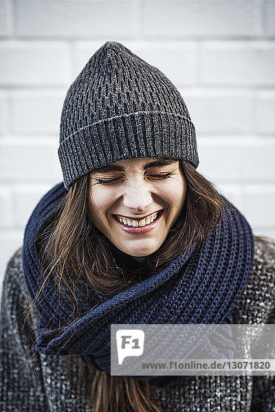 Cheerful woman laughing against brick wall