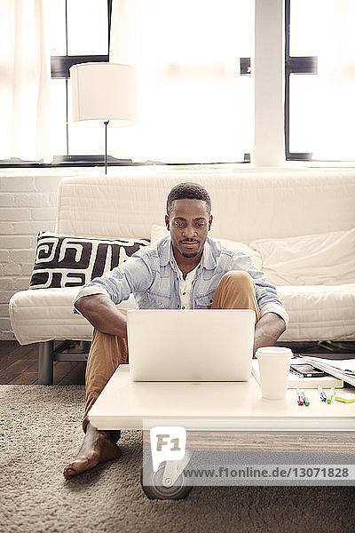 Mann benutzt Laptop-Computer  während er zu Hause im Wohnzimmer sitzt