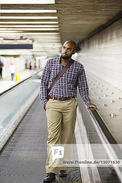 Mann schaut auf  während er auf der Rolltreppe am Bahnhof steht