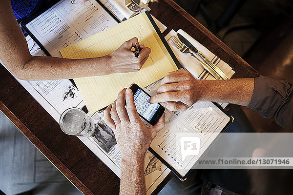 Overhead view of man using smart phone while sitting with girlfriend in restaurant