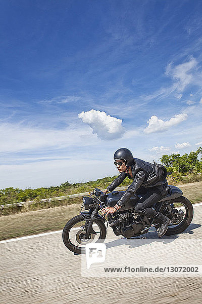 Mann fährt Motorrad auf Straße gegen bewölkten Himmel