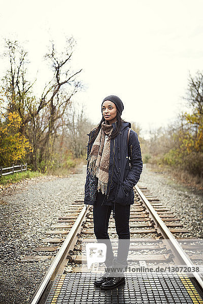 Nachdenkliche Frau steht auf Eisenbahnschienen vor klarem Himmel